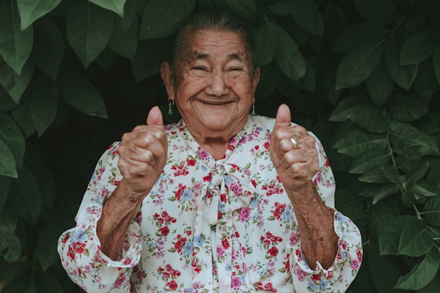 A smiling old woman gives two thumbs up.