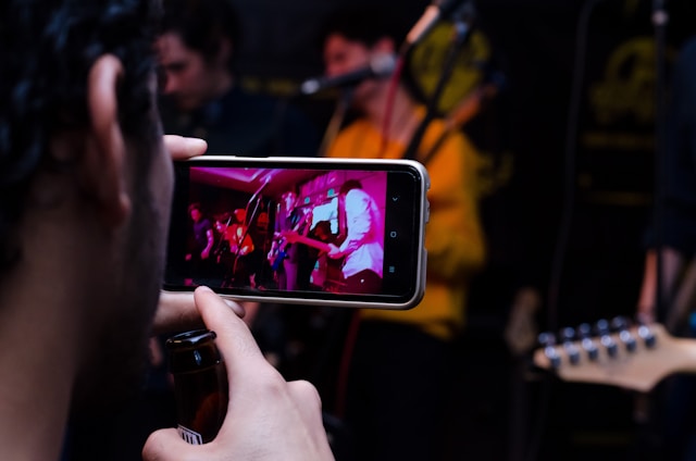 Someone uses a mobile phone to record a video of a band performing on stage.