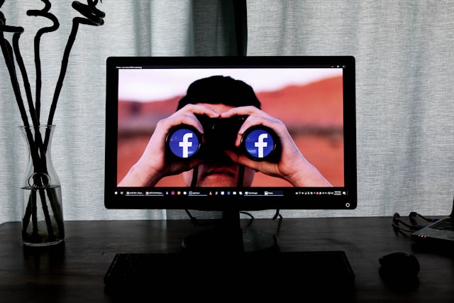 A computer screen displays a man looking through a pair of binoculars with the Facebook logo shown on both lenses.