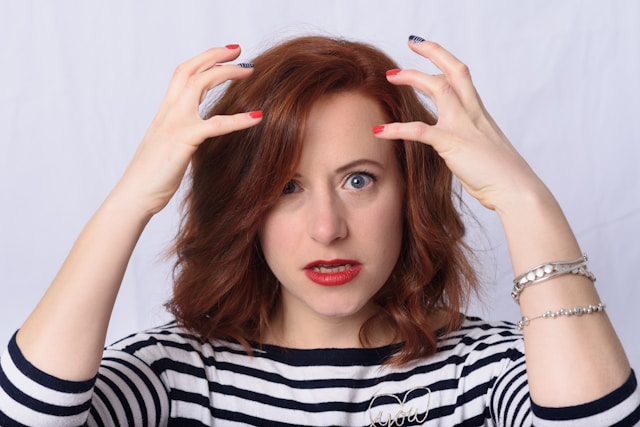 A woman in a black and white striped shirt has her hands over her head.
