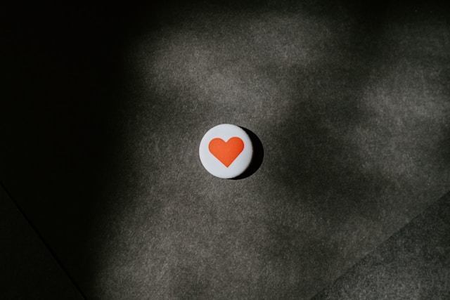 A round, white button with a red heart sits on a concrete surface.