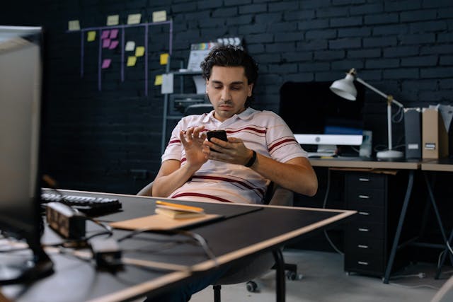 A man in a striped shirt scrolls on his phone.