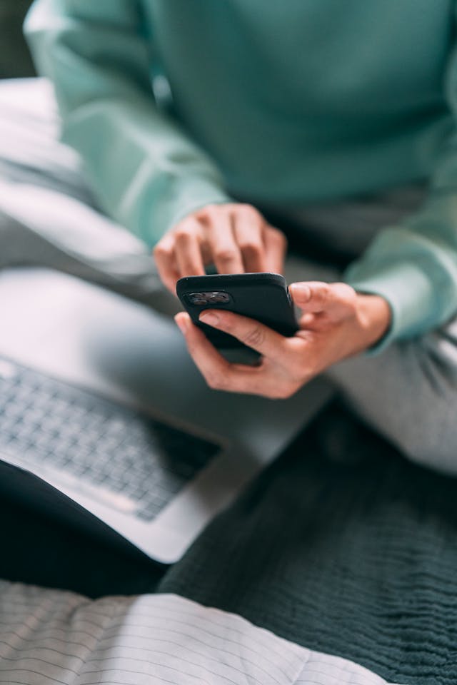 A person in a green sweater types on a phone.