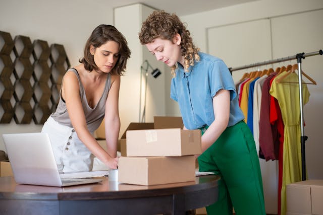 Two women package items into boxes.