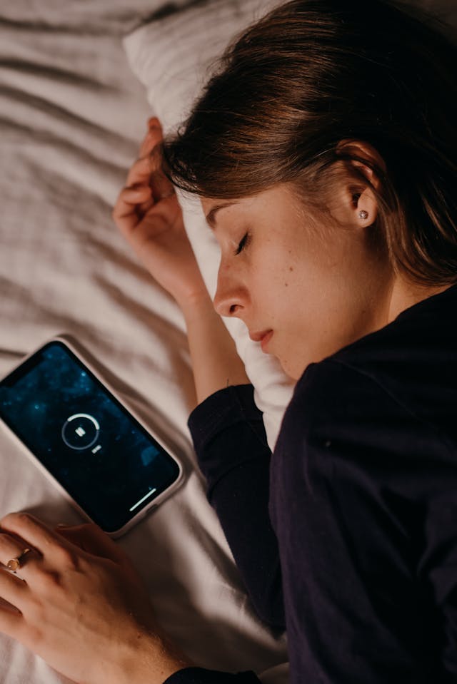 Woman limiting her screen time by resting her eyes while laying next to her phone.