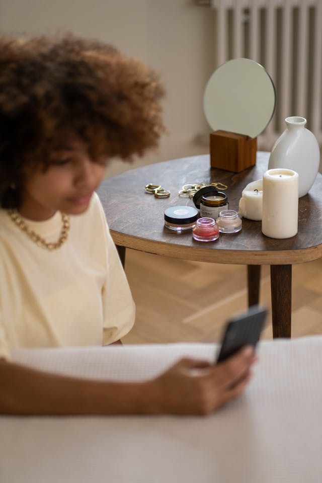 A woman scrolls on her phone with makeup in the background.