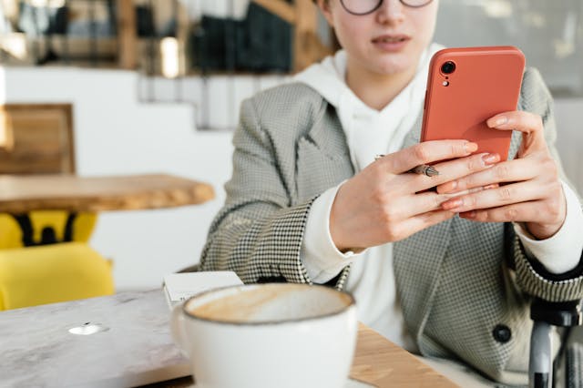 A woman with a mug of coffee types on her cell phone.