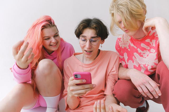 A group of people wearing pink gather around a cell phone.