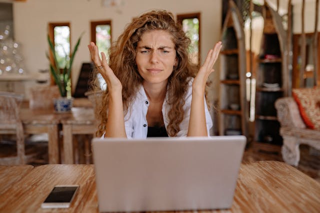 A woman sits in front of her laptop, visibly frustrated.