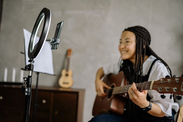 A woman records a video of herself playing a guitar.