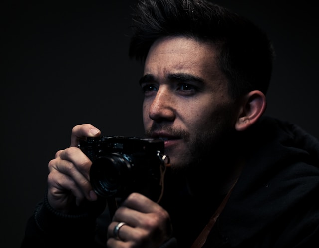A man looks forward while holding a digital camera.