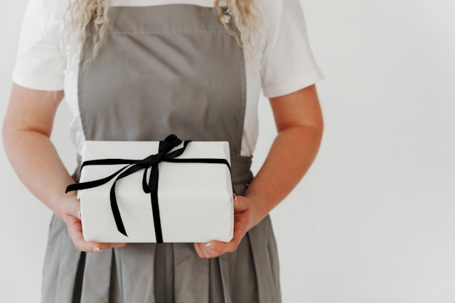 A woman holds a white gift box with a black bow around it.