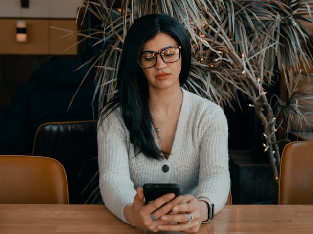A woman sits at a table and watches TikTok videos on her phone.