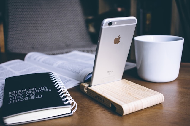 A white iPhone is set up on a phone stand on a table for TikTok viewing.