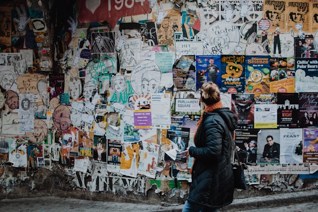 A woman looks at a wall covered with printed ads.