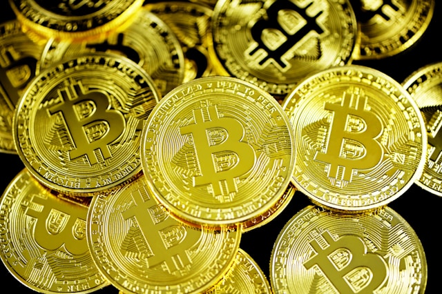 A pile of gold coins with an imprint of the letter “B” are scattered on a black table.