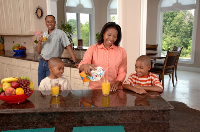 A husband smiles as he watches his wife pouring juice for their two sons.