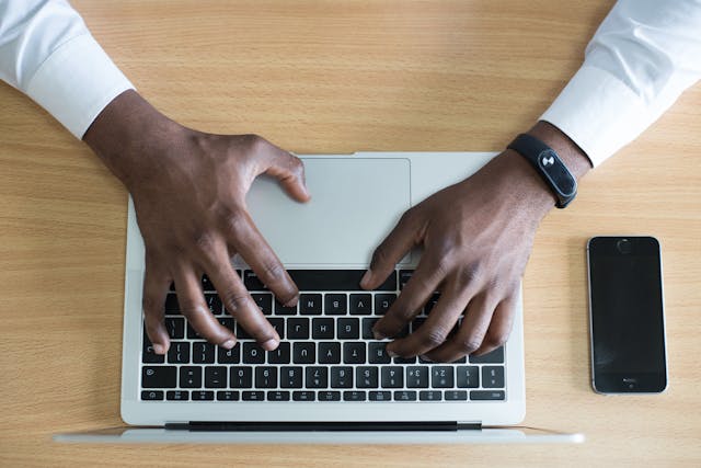Aerial view of a man’s hands typing on a laptop.