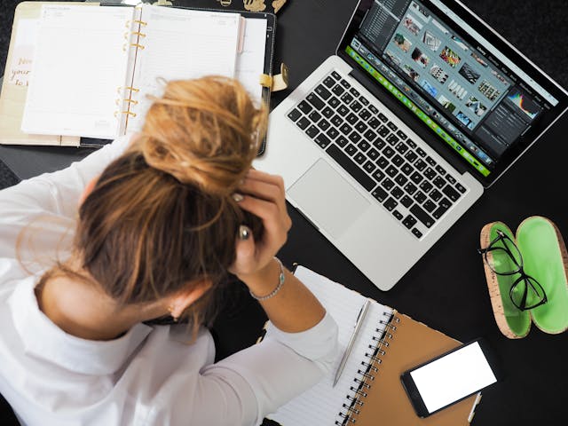 A woman sits in front of her Macbook with her head in her palms.