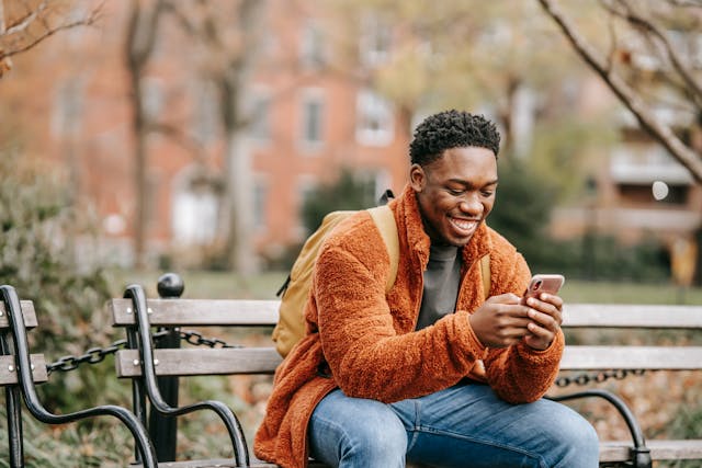 A man on a park bench happily uses his phone.