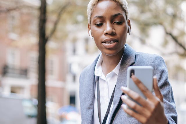 A woman wearing earbuds looks at her phone screen.