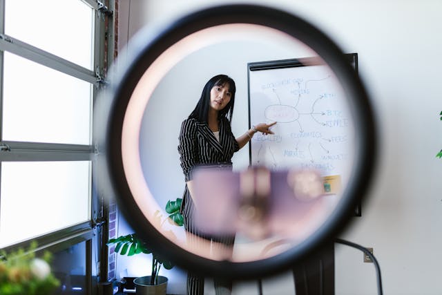 A woman explains something written on a whiteboard and records it.
