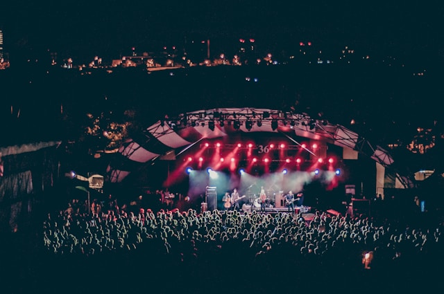 A big audience gathers around a stage at an outdoor concert.