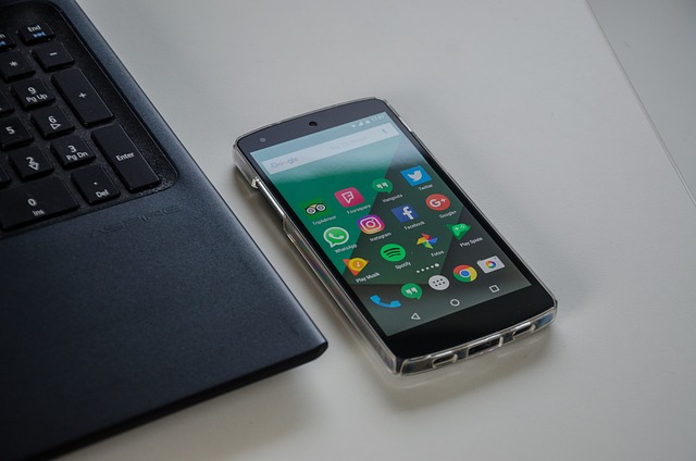 A smartphone next to a laptop displays several social media apps on the screen.