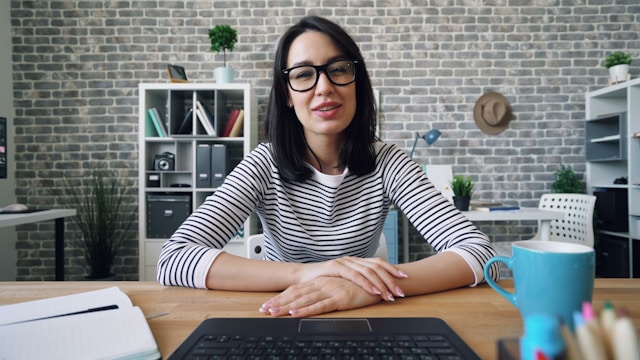 A woman sits in front of a laptop while she speaks to her audience in a TikTok video.