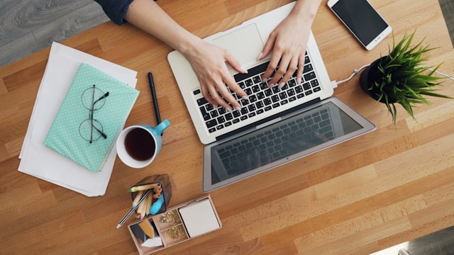 A person sits at a table and types on her laptop.