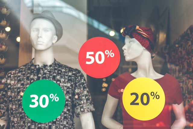 A store’s display window features two mannequins and discount offers.