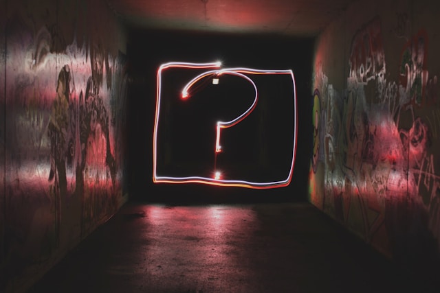 A dark room with a lit sign shaped like a question mark on a wall.