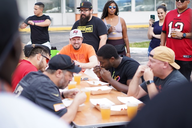 Men sitting around a table engage in a chicken-wing eating contest.