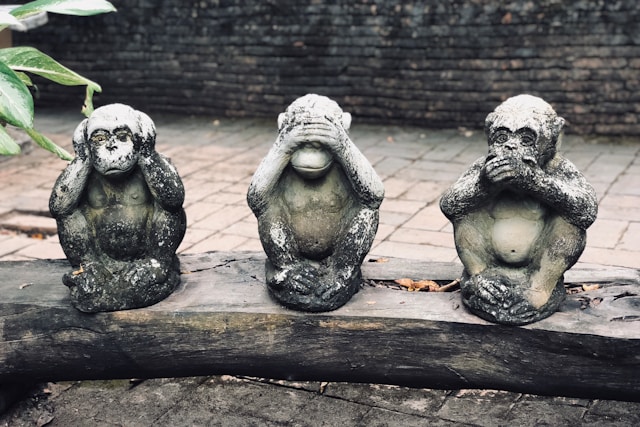 Statues of the three wise monkeys on a piece of log.
