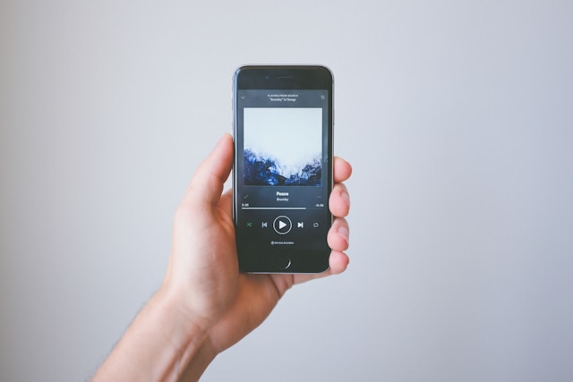 A person’s hand holds up a phone as it plays music.