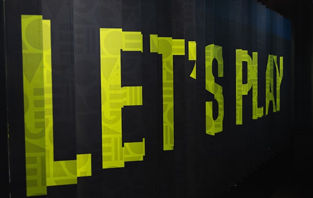 A green sign on a black wall reads, “Let’s Play.”