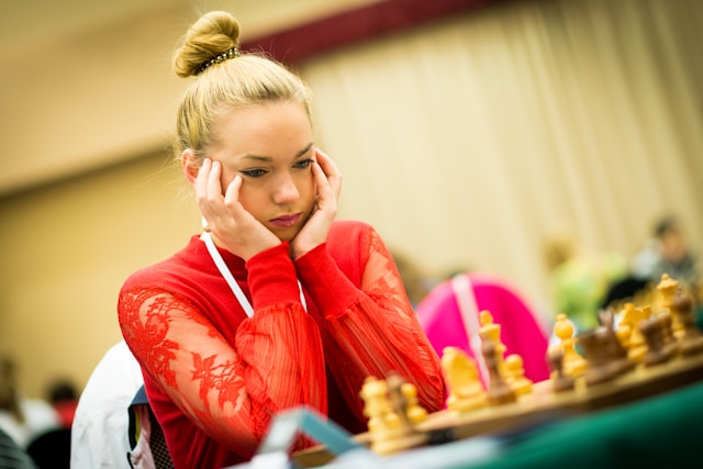 A chess player sits in front of a chessboard and thinks of her next move.