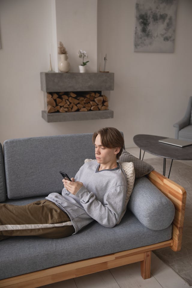A man lies on his couch while he uses his phone.