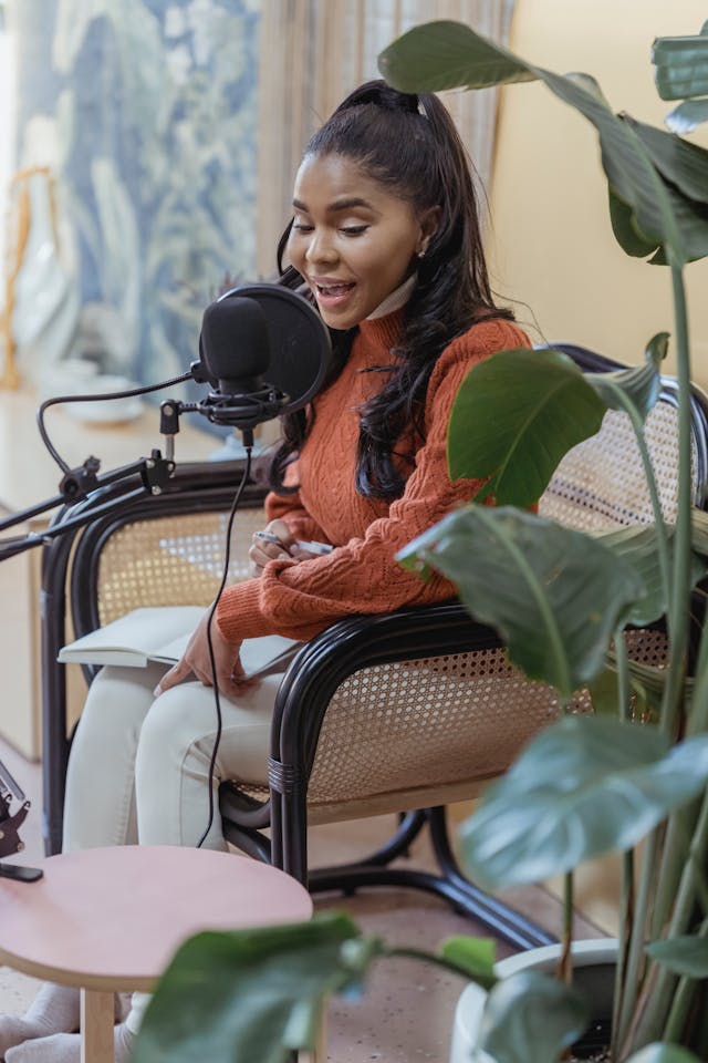 A young lady wearing an orange sweater speaks into a microphone.