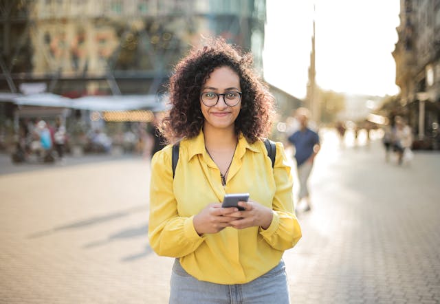 A woman in a yellow shirt smiles while using her phone.