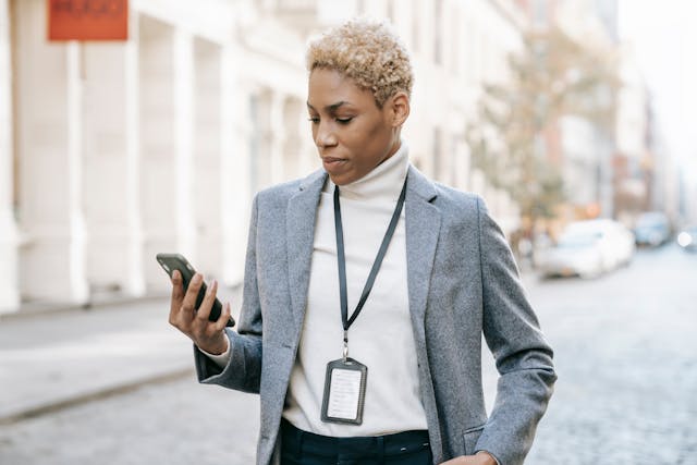 A woman in a gray blazer looks at her smartphone.