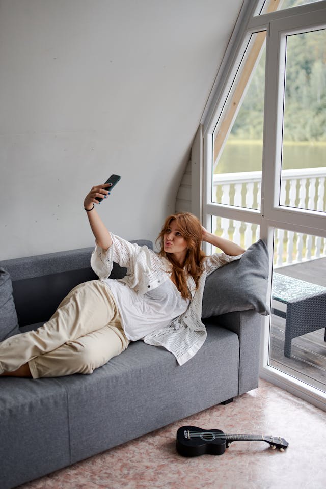 A woman takes a selfie of herself while lying on the couch.