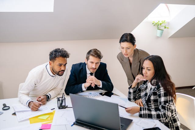 Four professionals gather around a laptop.