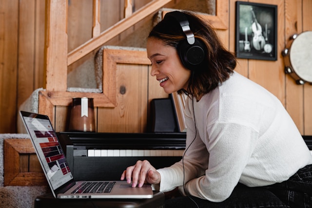 A woman wearing headphones browses through the music library on her laptop.