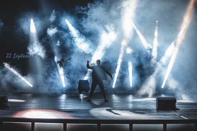 A man performs on a stage under numerous spotlights.