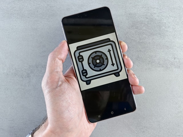 A phone screen shows a black and gray image of a wall safe/vault.