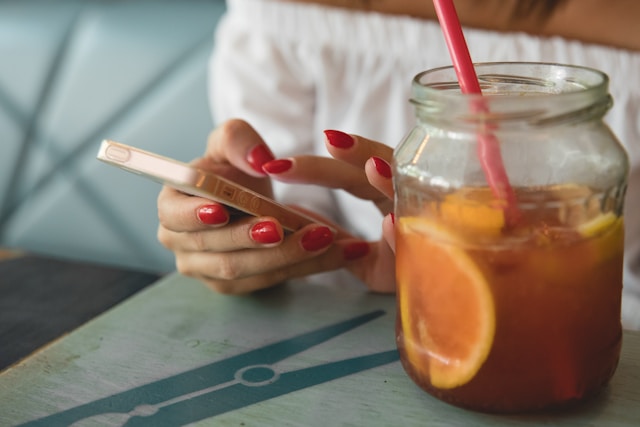 A woman edits a TikTok video on her phone while enjoying a jar of fresh orange juice.