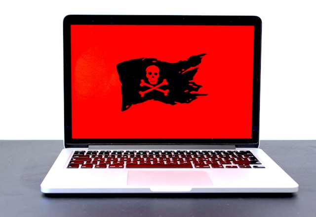 A laptop screen shows up red with a skull and two bones on a tattered black flag.