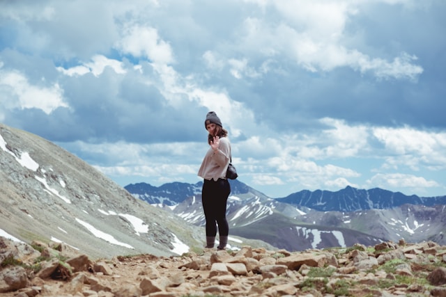 A woman stands on a hiking trail and waves goodbye.