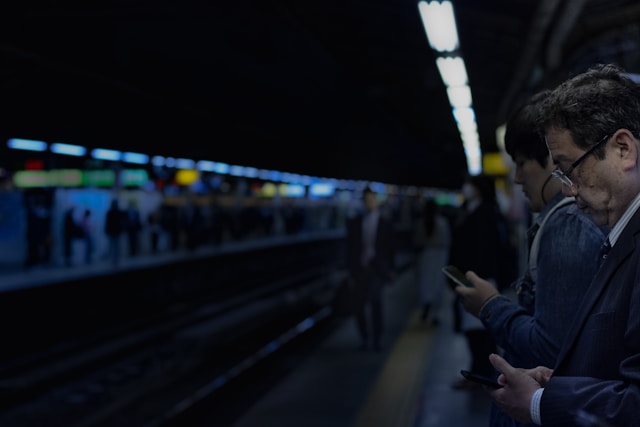 Commuters on a train platform browse the internet on their phones while they wait.